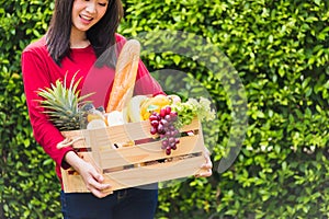 Woman farmer standing hold full fresh food raw vegetables fruit in a wood box