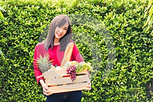 Woman farmer standing hold full fresh food raw vegetables fruit in a wood box