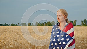 Woman farmer with usa flag on weeds walking along wheat field