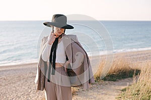 Woman in fashion clothes and hat at sunset beach.