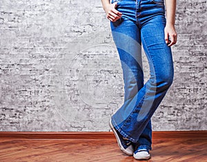 Woman fashion concept. Female legs in jeans and sneakers on gray wall background