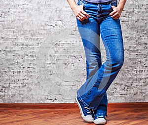 Woman fashion concept. Female legs in jeans and sneakers on gray wall background