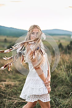 Woman fashion model portrait outdoors in the summer field, sunset. Boho style young woman in white dress and with