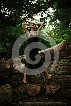 Woman in fashionable dress pose on tree trunk, fashion. Woman with makeup and long curly hair on nature, look. Fashion