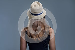 Woman in fashionable hat and black shirt from the back on gray background in studio. Sexy girl