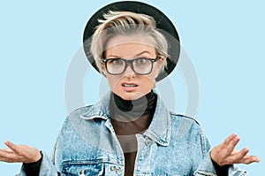 Woman in fashionable hat and glasses with displeased face expression on blue background