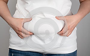 Woman with fat flabby belly, overweight female body on gray background. Woman in jeans and a light shirt is standing sideways and