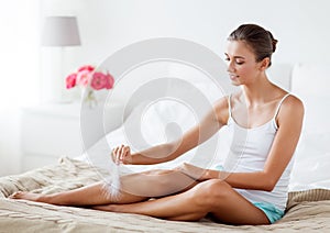 Woman with feather touching bare legs on bed