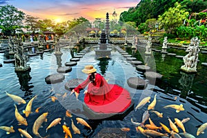 Woman feeding colorful fish in pond at Tirta Gangga Water Palace in Bali, Indonesia