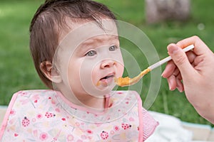 woman feeding her beautiful little daughter - mother hand and close up portrait of adorable and happy baby girl eating baby