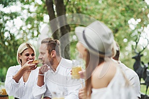 Woman feeds her husband with delicious sandwich outdoor with friends at daytime