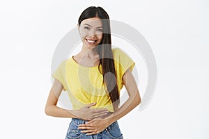 Woman feeling healthy and pleased. Delighted good-looking female with beautiful smile gazing at camera touching stomach
