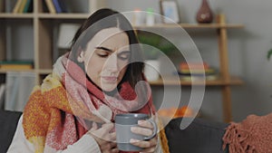 Woman feeling unwell holding cup and drinking tea at flat