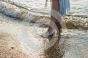 Woman feet in barefoot touched by gentle sea surf waves on sand beach