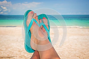 Woman feet with blue flip flops, beach and sea