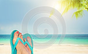 Woman feet with blue flip flops, beach and sea in the background, summer concept