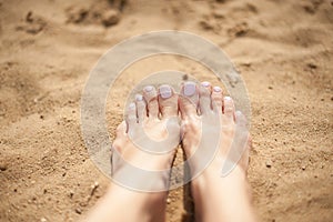 Woman feet with light pink toenails on the sand