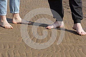 Woman feet and man feet barefoot standing opposite each other on the sand beach