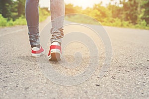 Woman feet with red sneaker shoes walking on the roadside.