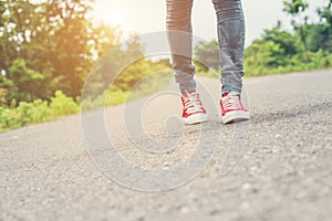 Woman feet with red sneaker shoes walking on the roadside.