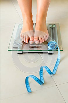 Woman feet standing on bathroom scale and tape