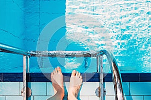 Woman feet standing near the stairs in swimming pool