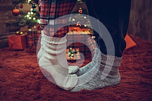 Woman feet standing in tip toe in winter socks on male lags on a fluffy red blanket near a Christmas tree with gifts. Concept.