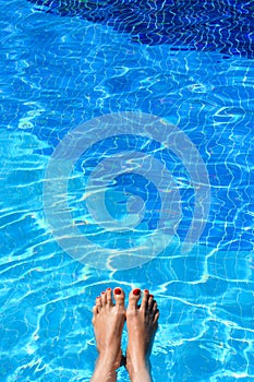 Woman feet in swimming pool on a hot summer day