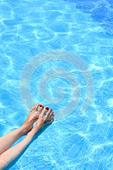 Woman feet in swimming pool on a hot summer day