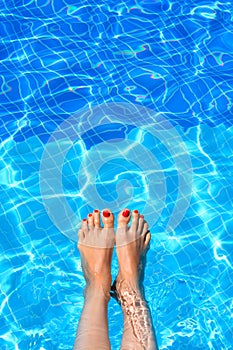 Woman feet in swimming pool on a hot summer day