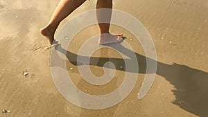 Woman feet walking on the wet sand of the beach entering the water in slow motion