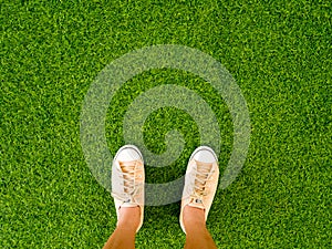 Woman feet wear vintage soft brown sneaker shoes stand on green grass floor