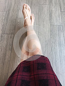 Woman feet wearing pink sandals and scot dress of fashion. Selfie of feet and legs in pink shoes on wooden background photo