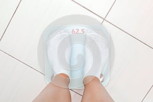 A woman feet in white socks are on an electronic scale in the bathroom, she is overweight and she wants to lose weight