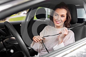 woman or female car driver fastening seat belt