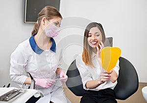 Woman with female dentist checking their teeth at mirror after dental procedure in dental clinic. Dentistry