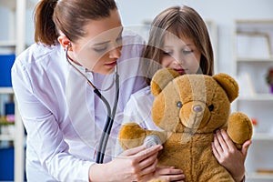 The woman female doctor examining little cute girl with toy bear