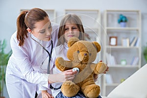 The woman female doctor examining little cute girl with toy bear