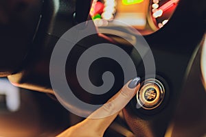Woman female finger pressing the Engine start stop button of a car.