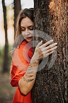 Woman with fern tattoo hugging trees and enjoying nature in the pine forest.