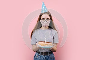 Woman in festive cap and medical mask holding birthday cake