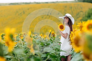 Woman in the field of sunflowers. A happy, beautiful young girl in a white hat is standing in a large field of sunflowers. Summer