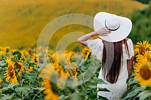 Woman in the field of sunflowers. A happy, beautiful young girl in a white hat is standing in a large field of sunflowers. Summer