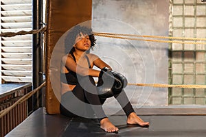 Woman fighter girl power. African american woman fighter with boxing gloves sitting on boxing ring waiting and resting