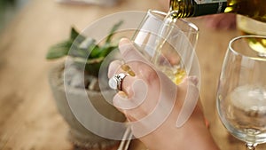 Woman fill glasses of her friends pouring white wine in sea view restaurant. Female hands hold bottle of alcohol drink