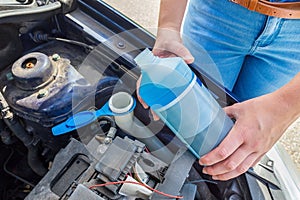 Woman filling car reservoir with blue fluid in bottle