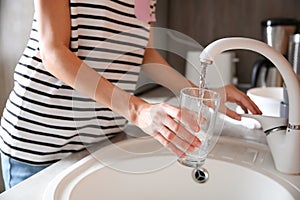 Woman filling glass with water from faucet in kitchen