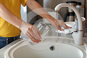 Woman filling glass with water from faucet in kitchen