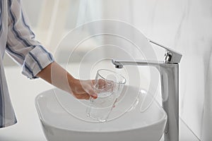 Woman filling glass with water from faucet over sink, closeup