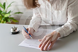 Woman filling hotel reservation form. Silver vintage bell on reception desk. Hotel service, registration.